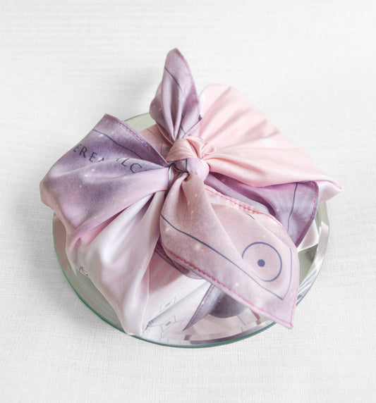 A pink and white vegan silk altar cloth with a geometric pattern, tied in a knot on a circular object, likely a tray or table.